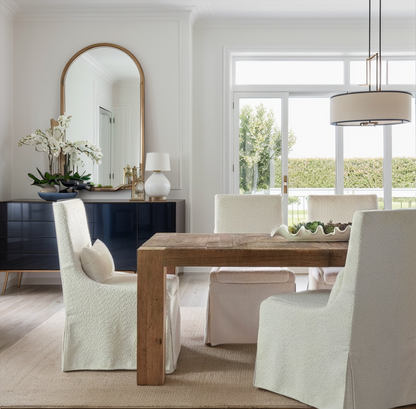 Dining room with wooden table and white chairs, large mirror on the wall.
